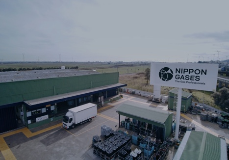 Exterior view of a Nippon Gases industrial facility with warehouses, a truck loading area, and storage equipment.