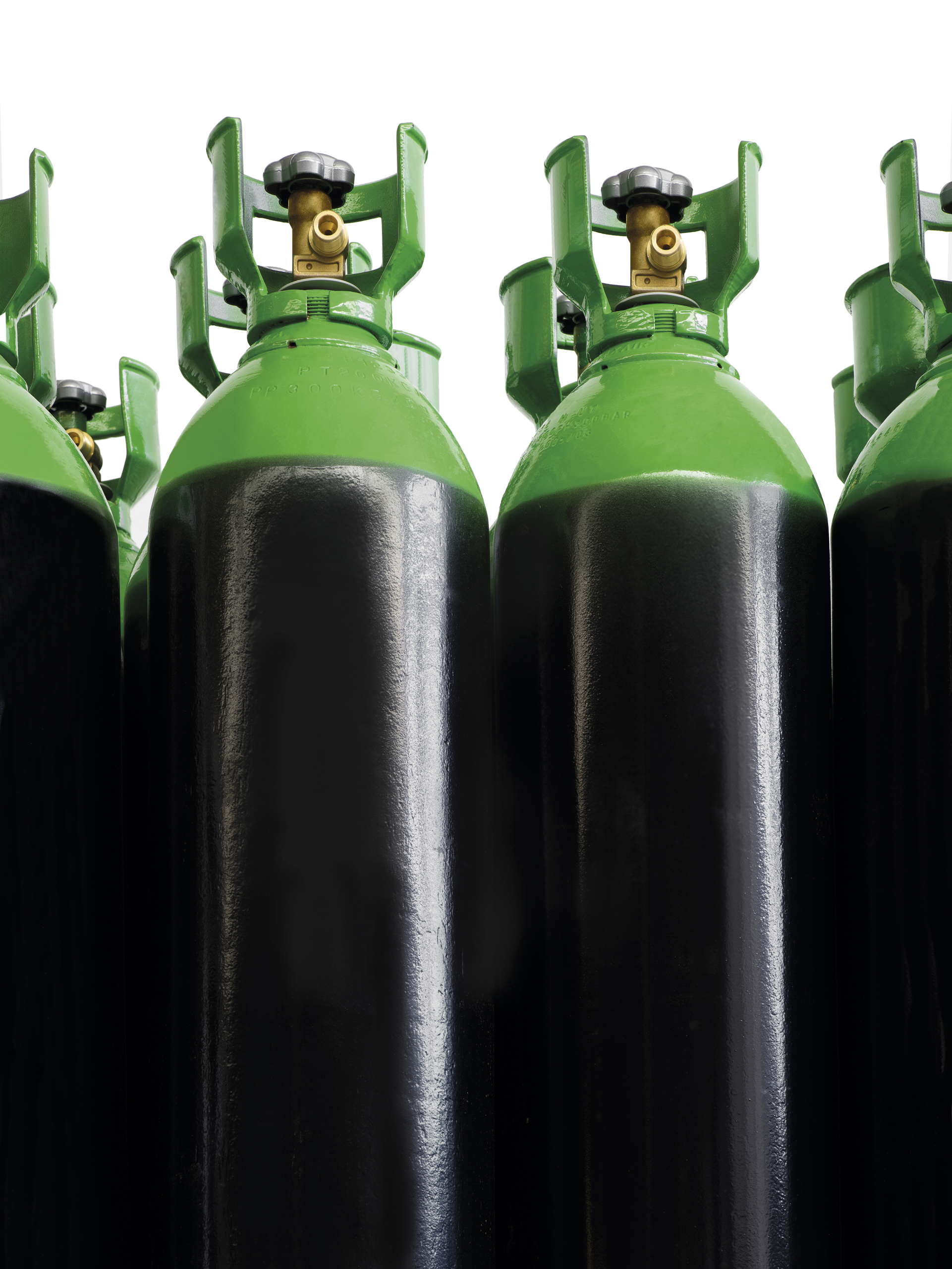 Group of industrial gas cylinders with black bodies and green tops, viewed from a low angle against a white background.