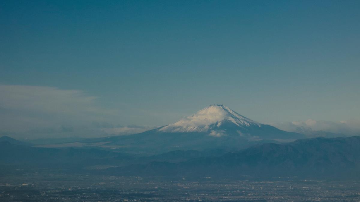 Distant view of a snow-capped mountain rising above a valley under a clear blue sky.
