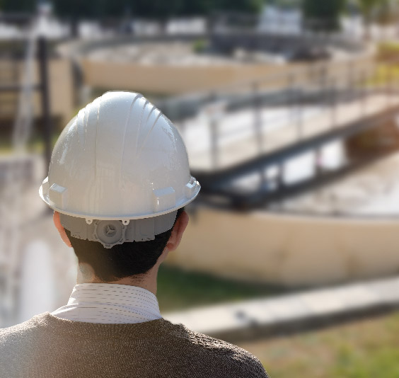 Person wearing a white hard hat overlooking an industrial water treatment facility.