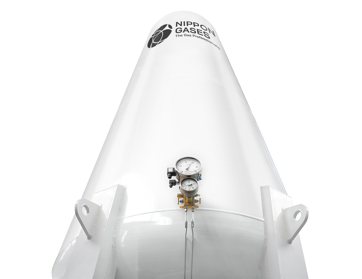 Large white cryogenic storage tank with pressure gauges and the Nippon Gases logo, photographed from a low angle.